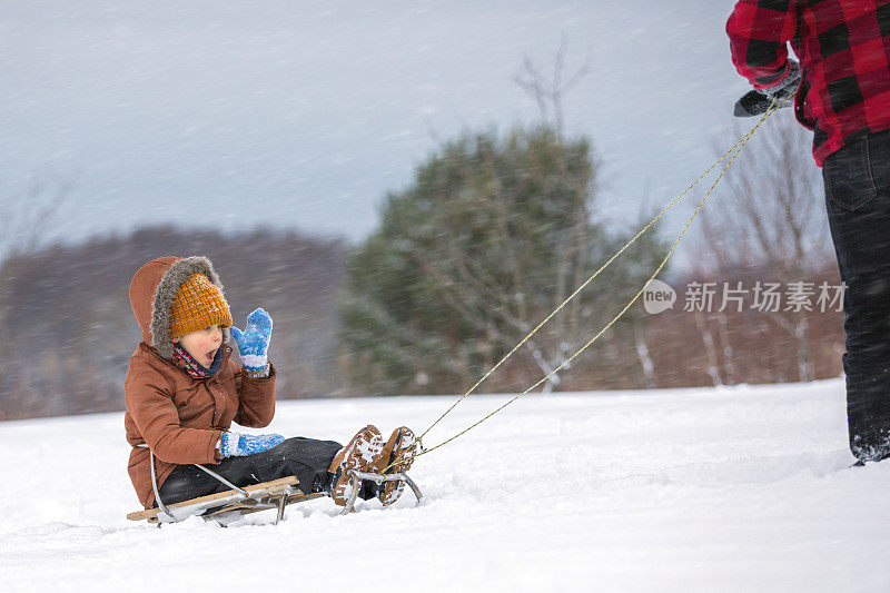 一个小男孩和他的父亲在厚厚的雪中旅行，雪橇被困在厚厚的雪中，外面有很强的暴风雪，天气很糟糕
