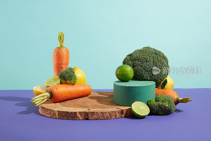 各种各样的蔬菜和水果放在蓝色背景的紫色桌子上，空的圆形讲台和木制托盘供展示。烹饪产品的正面照片