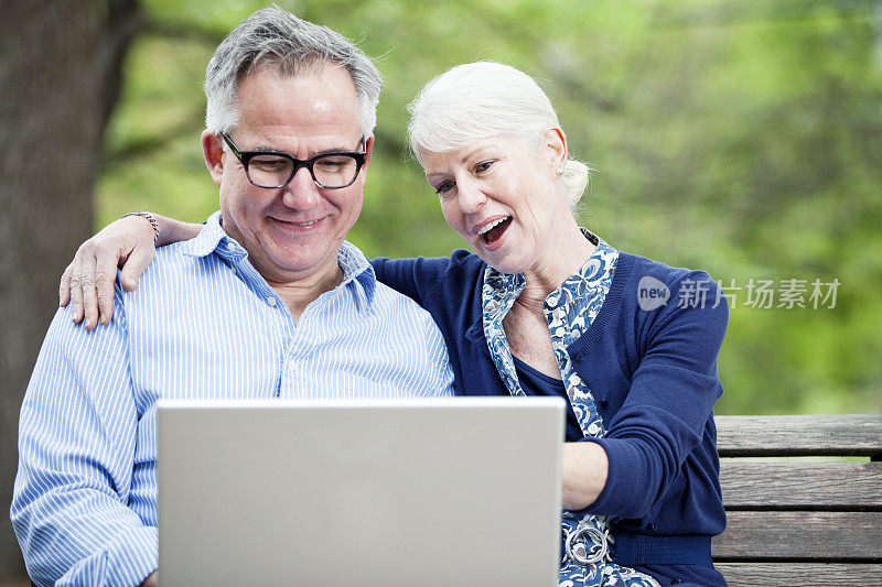 在城市公园里拿着笔记本电脑的老年夫妇