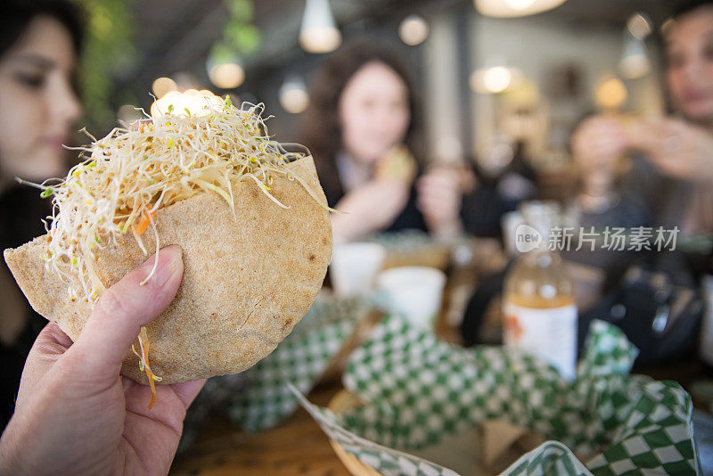 在餐馆里，女士手里拿着一个素食皮塔饼三明治。