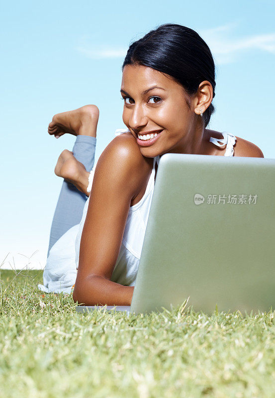 甜美的年轻女性在草地上休息时使用笔记本电脑
