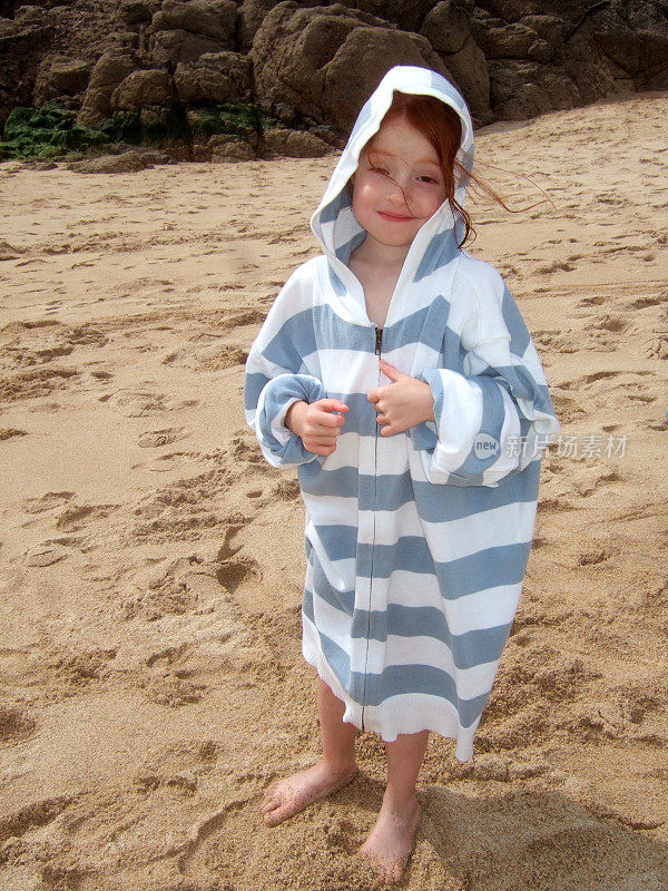 小女孩穿着爸爸的超大号连帽衫站在沙滩上