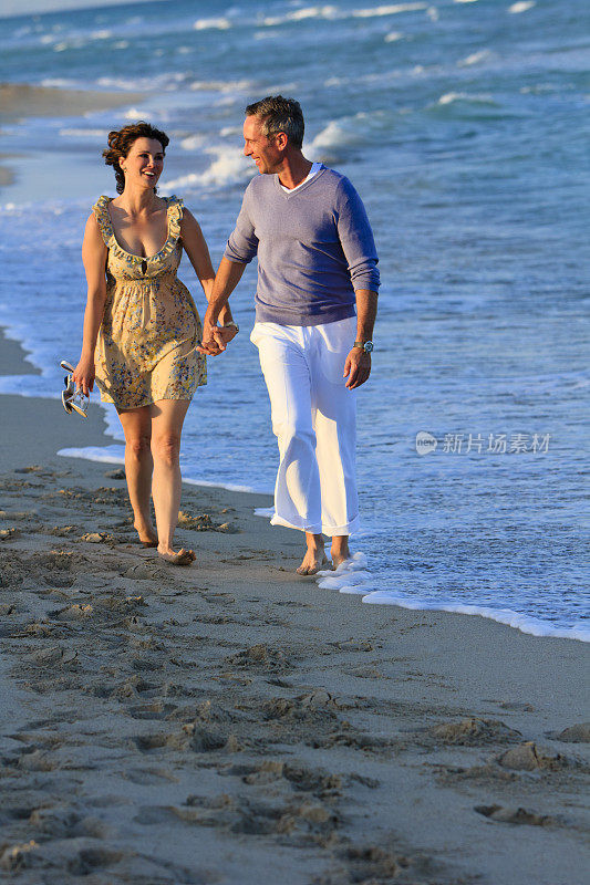 一对成年夫妇手牵着手在海滩上散步