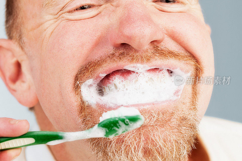 胡子成熟的男人微笑着，一边刷牙一边喷着牙膏