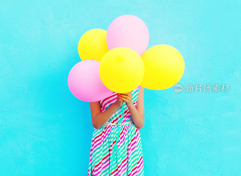 快乐的女人是隐藏她的头一个空气彩色气球在一个蓝色的背景有乐趣