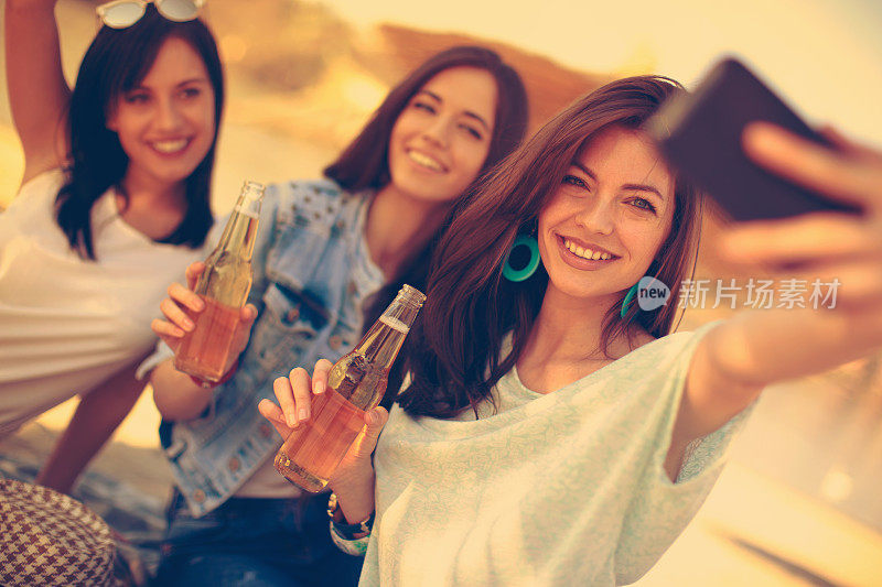 三个年轻女人在海滩上喝啤酒自拍
