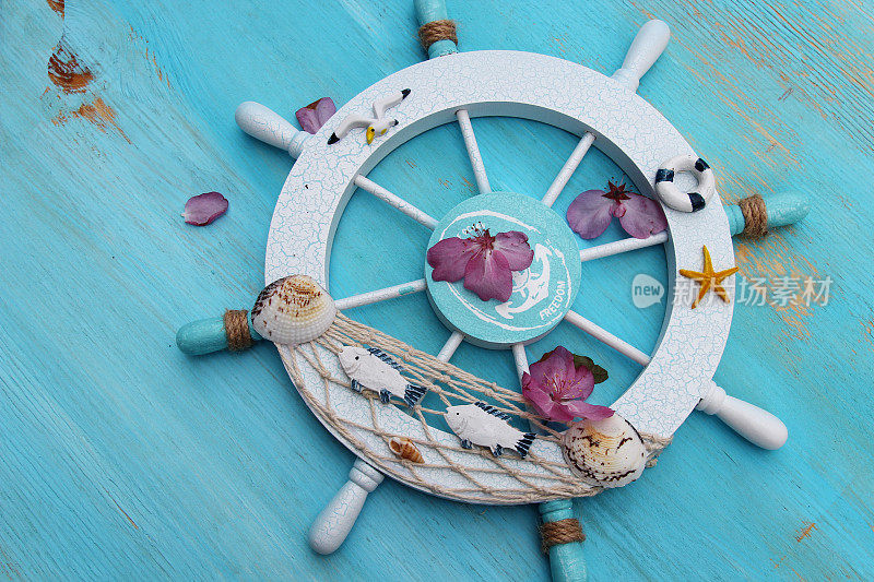 木制的船或船，方向盘，渔网，贝壳与花瓣在一个木制的蓝色背景