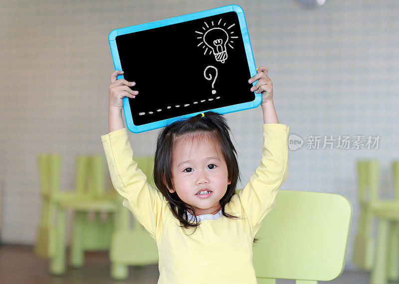 可爱的小女孩拿着画有虚线和灯泡图案的黑板在儿童房。教育的概念。