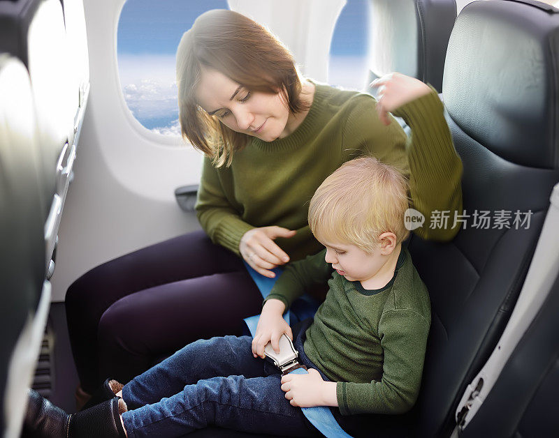 一位年轻的母亲在乘飞机旅行时帮助她的小儿子系上安全带