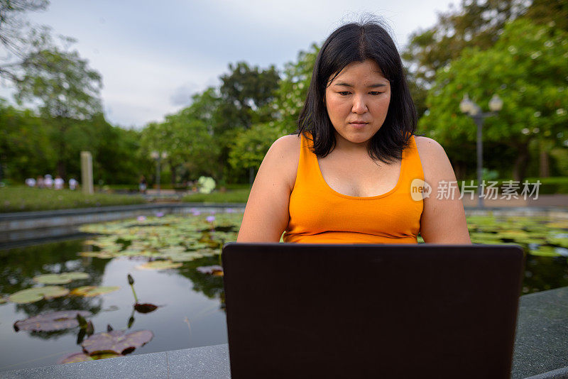 肖像超重的亚洲妇女穿着黄橙色的衣服放松在曼谷的公园在泰国