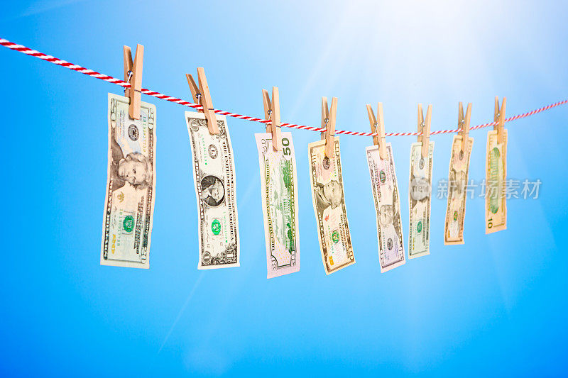 洗钱概念:把一排钞票别在晒着阳光的晾衣绳上