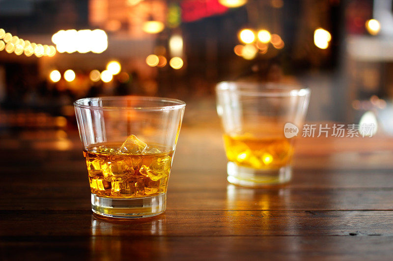 威士忌酒杯和冰块在彩色的夜晚酒吧的木桌上喝