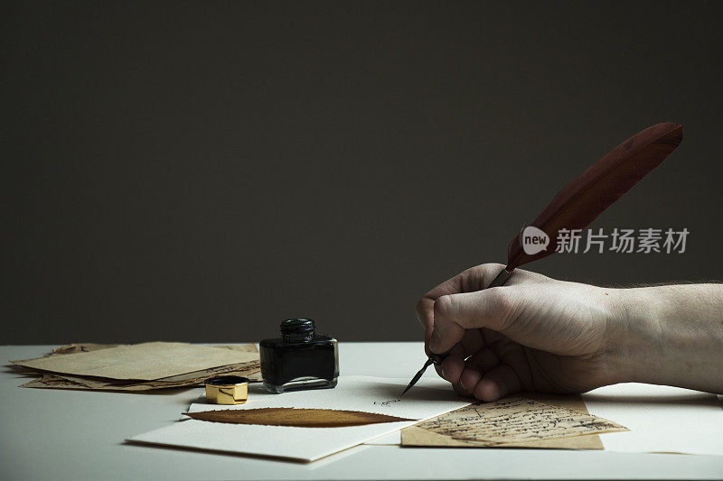 一张男人用古董笔、旧纸和墨水瓶书写信件的照片