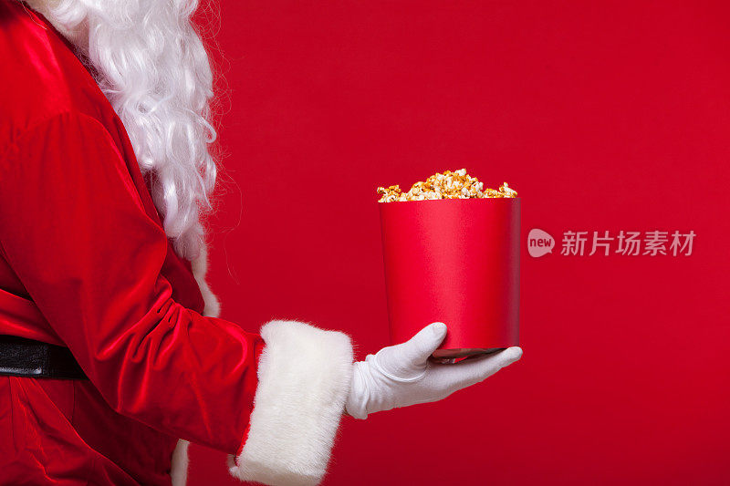 圣诞节。圣诞老人戴着手套的手与一个红色的桶爆米花，在红色的背景