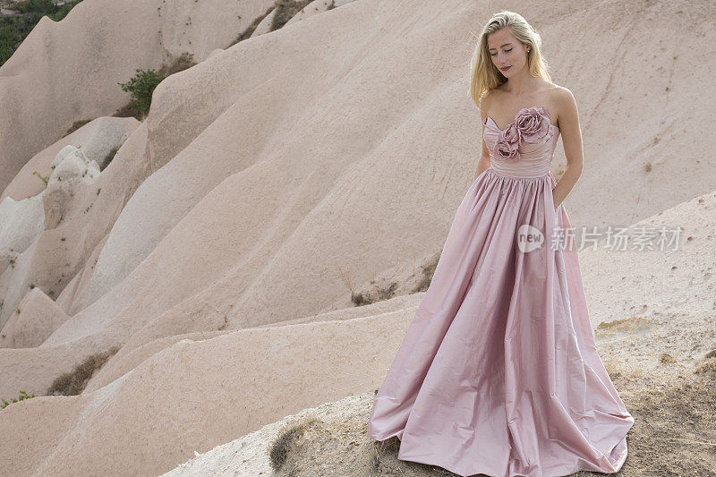 在卡帕多西亚，一名年轻女子穿着粉红色裙子在沙漠中拍照。