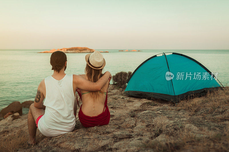 一对年轻夫妇坐在帐篷附近的海滩上，欣赏美丽的日落