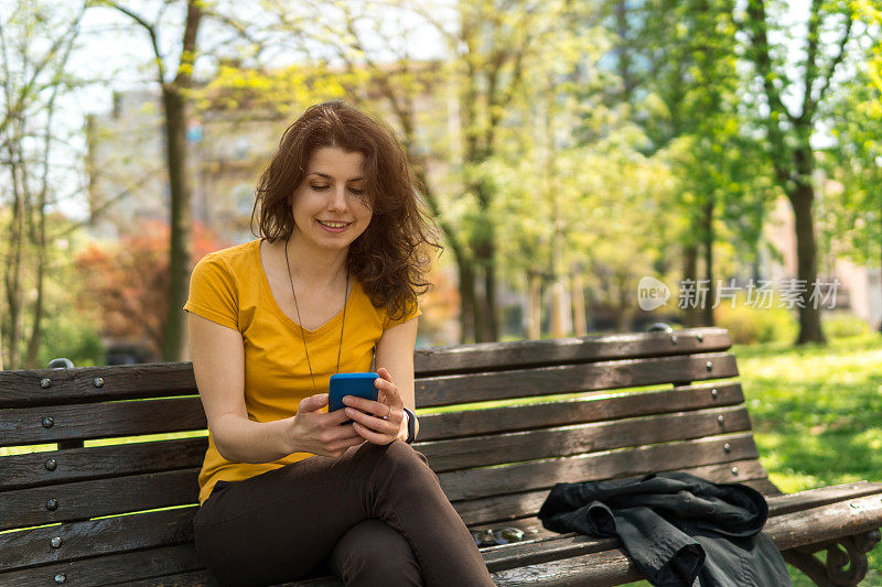 年轻漂亮的白人女孩在长凳上玩手机