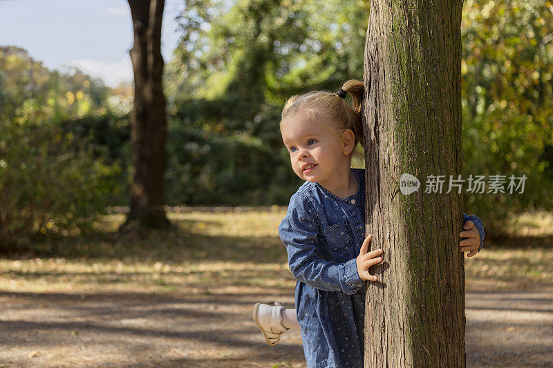 美丽的小女孩躲在树后面