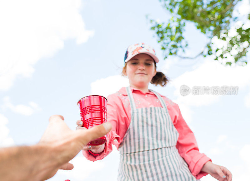 一个年轻女孩在她的柠檬水摊前给顾客递柠檬水