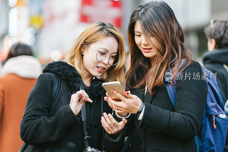 两个年轻的亚洲女游客在街上查看智能手机