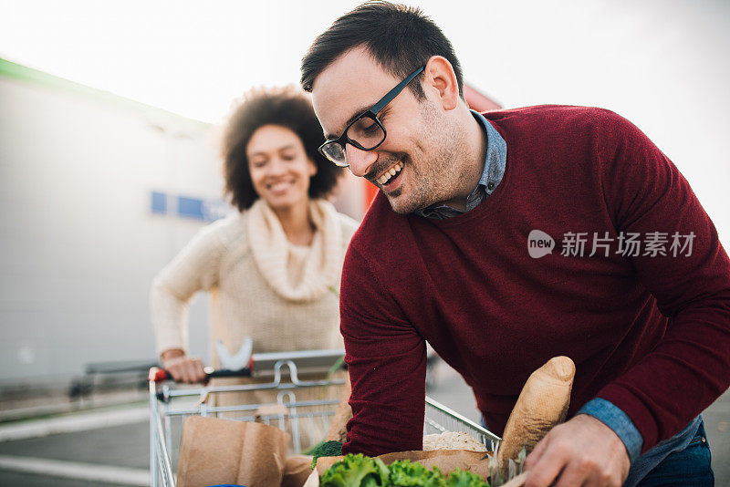 微笑的男子把杂货放进购物车