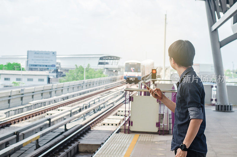 亚洲男子乘客使用智能手机在火车站看BTS，在BTS轻轨站等待。
