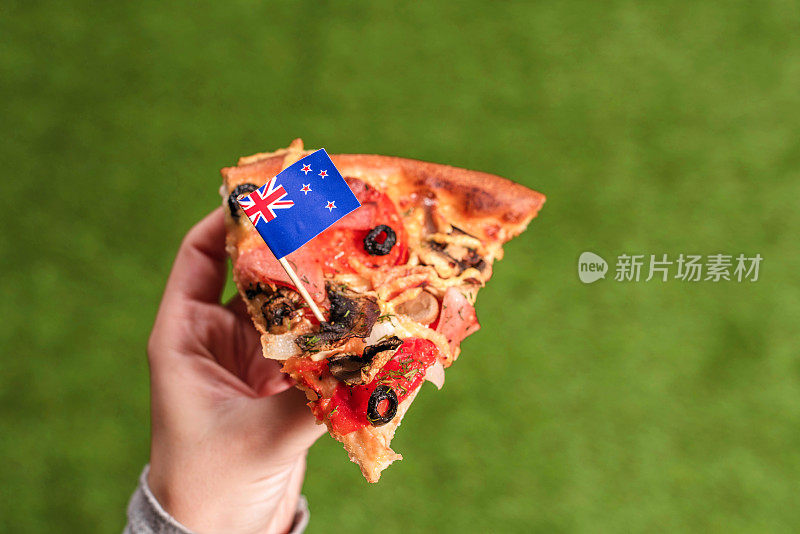 女性手里拿着一块披萨，上面插着澳大利亚国旗，形状是牙签。午餐在绿色的草地上。澳大利亚。概念
