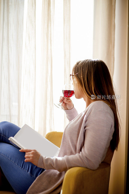 一个年轻的女学生拿着一本书坐在椅子上学习。拿着酒杯。