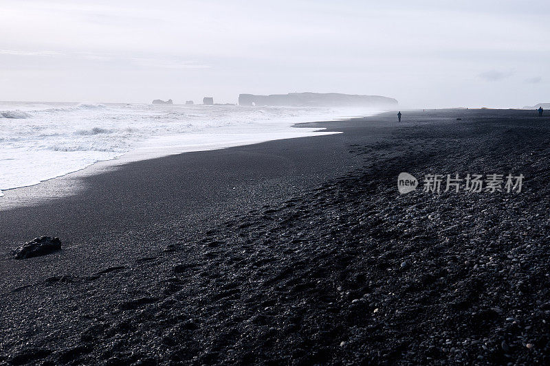 美丽偏远的海滩与黑色火山沙，冰岛维克。人们在远处拍摄大西洋的巨浪和岩层