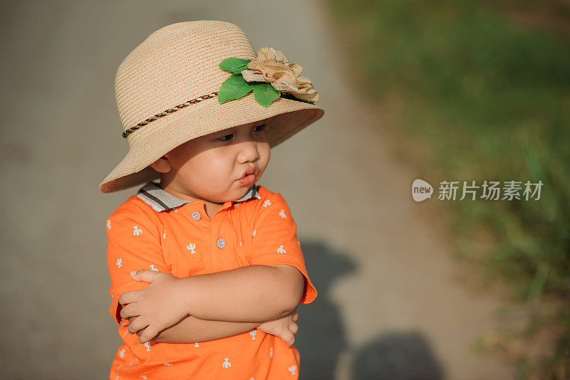 一个戴着草帽的亚洲华人小男孩在稻田里展示了可爱的脸