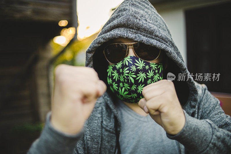 一幅在自家院子里戴着面具的男子肖像——以大麻叶为主题的防护面具——预防街道和花园周围空气中的冠状病毒或冠状病毒19的细菌感染