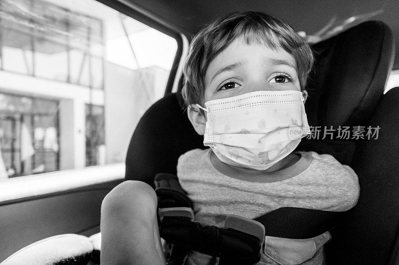 一个吓坏了的小男孩戴着防护面罩坐在汽车座椅上