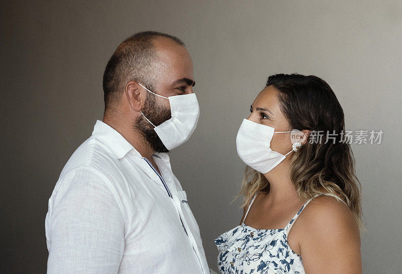 一对相爱的情侣戴着医用口罩，站在灰色的背景下