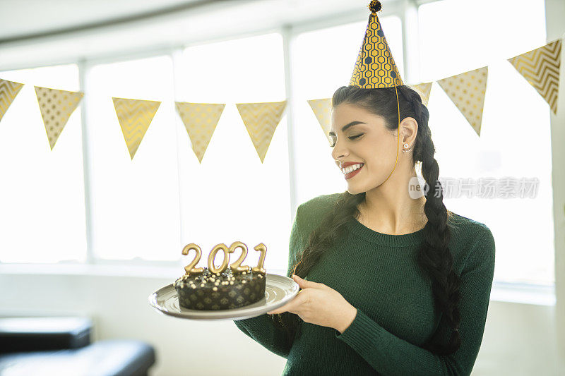 一名年轻女子在家庆祝圣诞节，手里拿着巧克力蛋糕，蛋糕上插着2021年的蜡烛