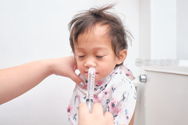 亚洲父母用注射器冲洗她生病的快乐的微笑可爱的小女婴的鼻子，用于鼻腔冲洗，盐水冲洗(鼻盐水或冲洗)和孩子