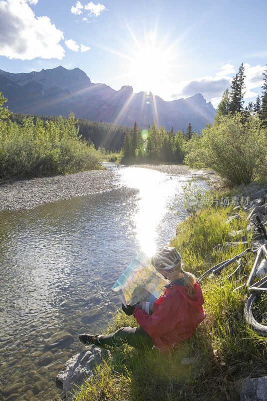 一个骑自行车的女人在日出时查看河岸上的地图