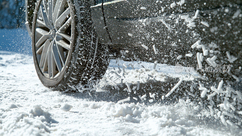 近距离:大块的雪飞在空中，因为汽车试图启动在积雪的道路上。