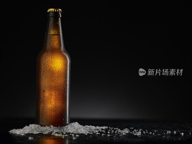 冰冷的棕色啤酒瓶上覆盖着冰和水滴-凝结。空白饮料饮料产品设计模型。站在黑色的桌子上，黑色的背景。