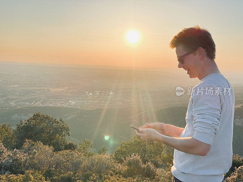 年轻人在阳光明媚的山脊上用手机，日出