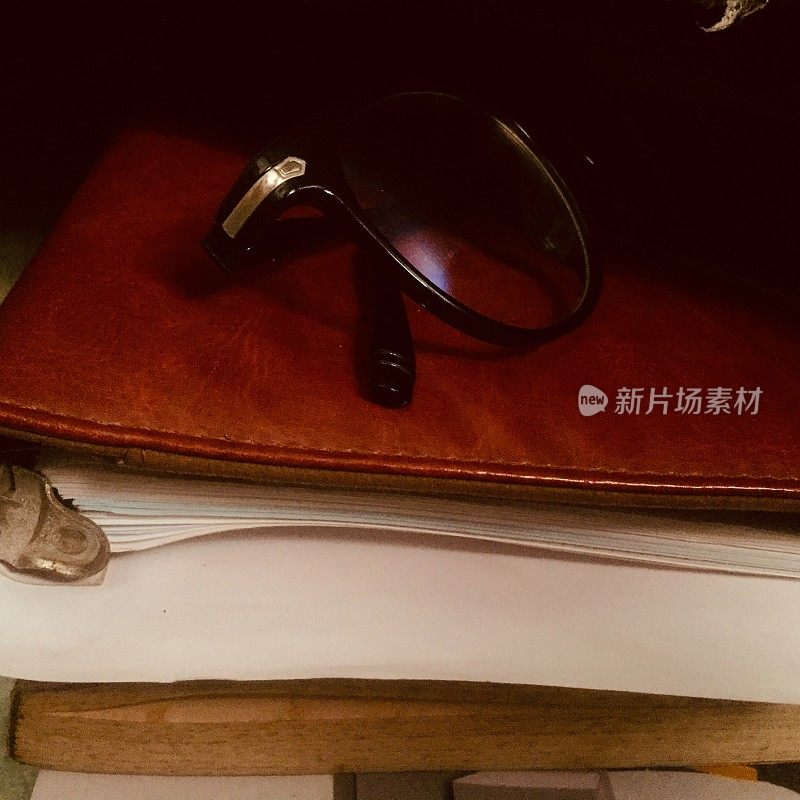 一副黑手把的眼镜放在一本皮革封面的旧书上，书在黑暗中。