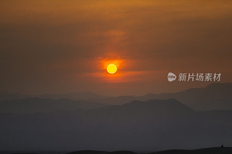 明亮的橙色太阳落在沙漠的山脉后面，森林大火的烟橙色的天空