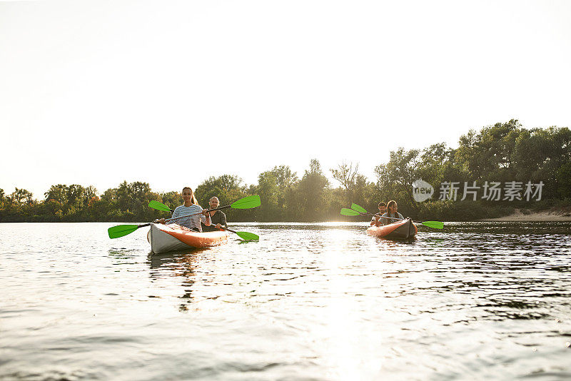 热情的年轻朋友们一起在河边划船，在夏天的一天在户外度过周末