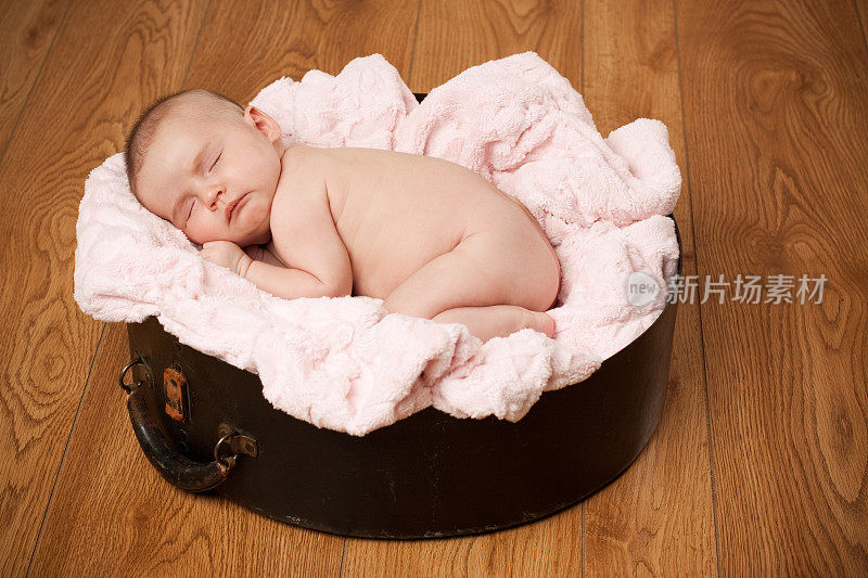 新生婴儿睡在粉红色的毯子木地板背景