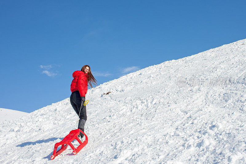 可爱的女人拉着红色的雪橇