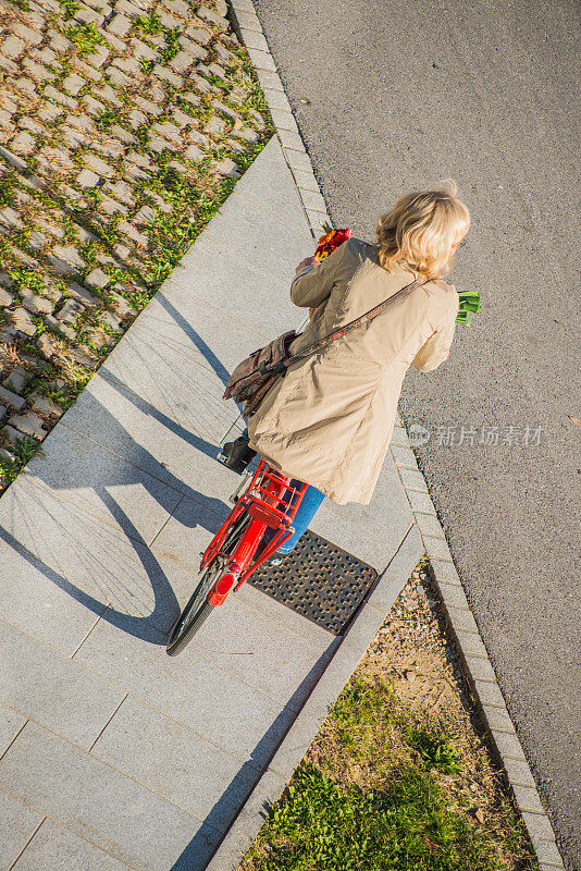 年长妇女骑自行车在城市，高角度的观点