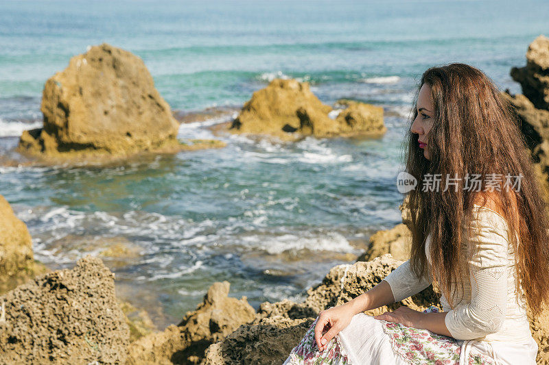 坐在海边岩石边沉思的女人