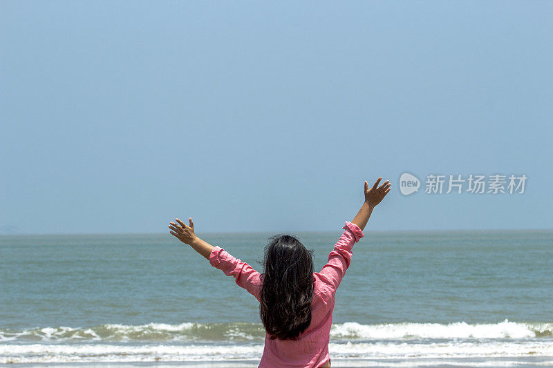 女孩在海滩上挥手，面朝大海