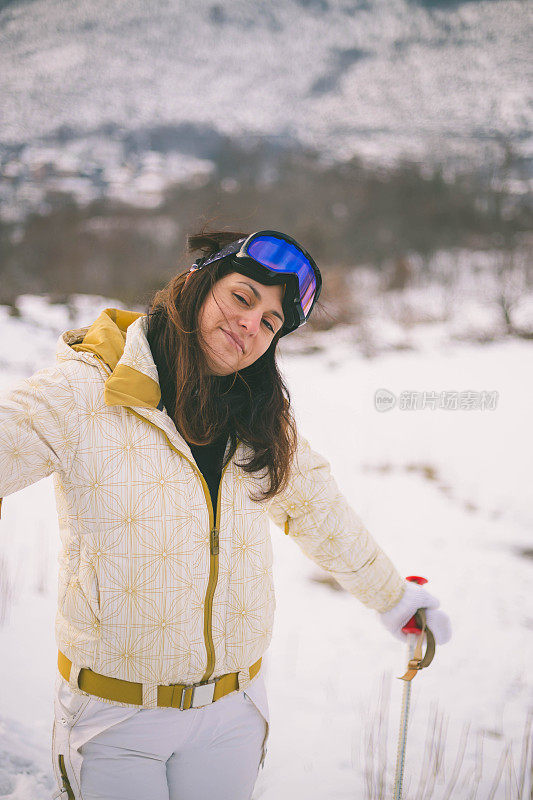 近景美丽的年轻女子在冬天的衣服站在一边，手拿木棍的背景雪山