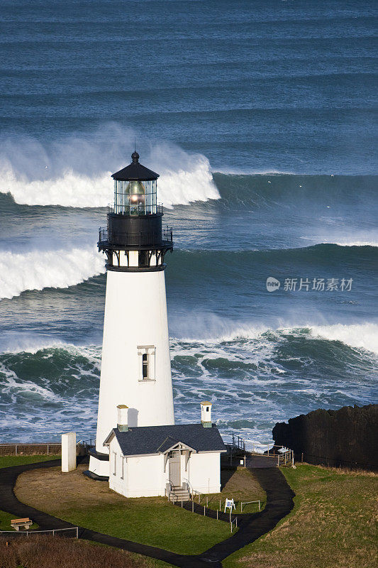 Yaquina头灯塔垂直特写，海浪在灯塔后面坠毁