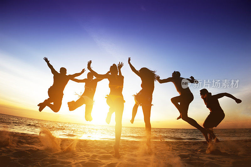 快乐的朋友跳跃海滩夕阳。友谊或团队概念